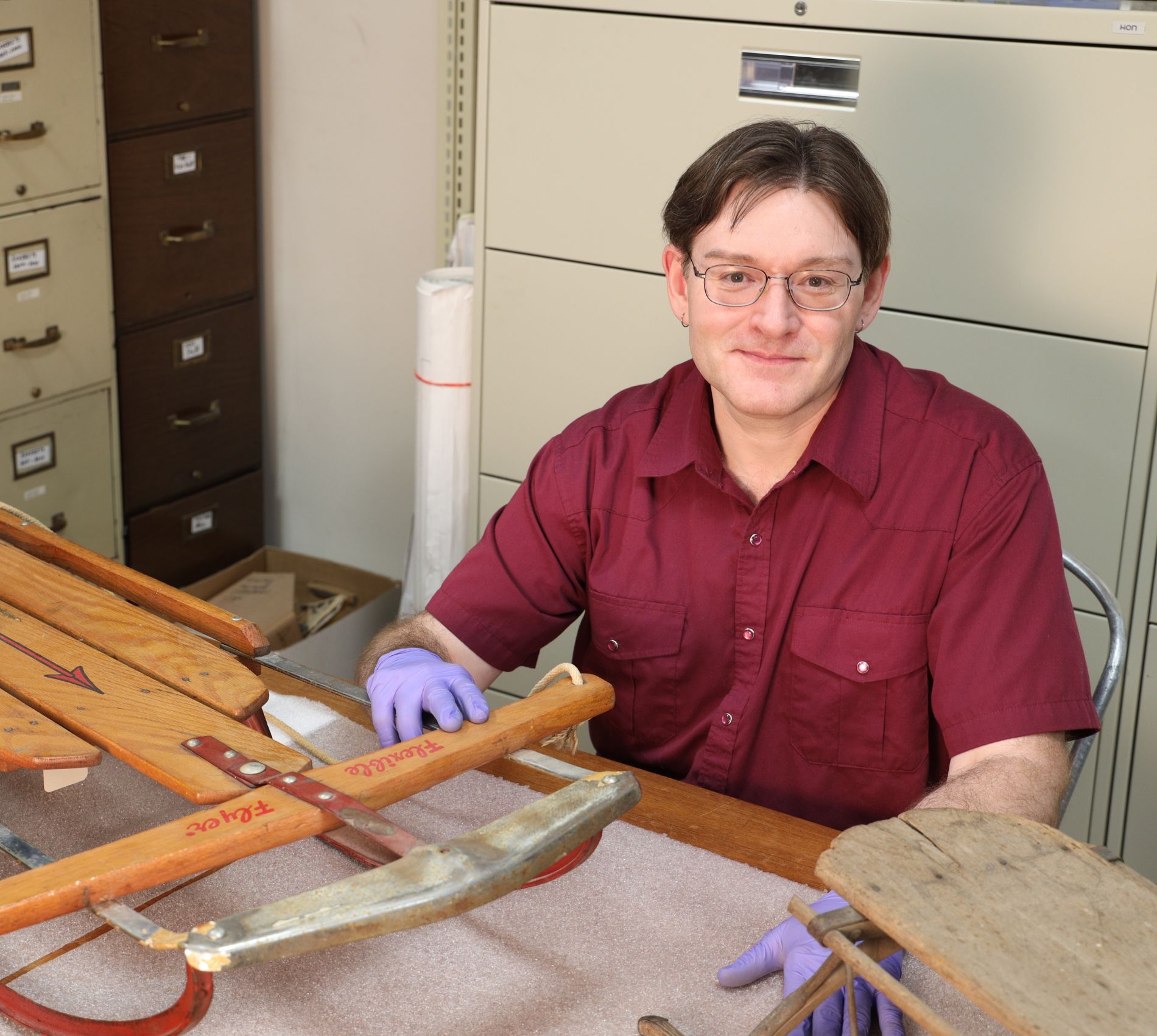 A man wearing gloves sitting at a table with a sled on it