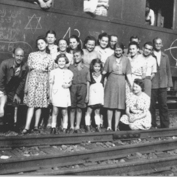 A black and white photo of a large group of people standing in front of a train.